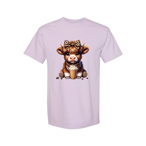 Dixie Magnolia Market light purple graphic tee with a cute Highland cow wearing a leopard print bow and bandana, holding an iced coffee.